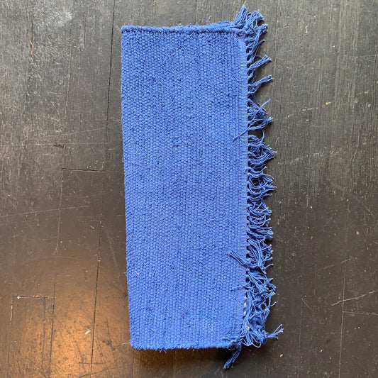 Blue fabric sample with frayed edges on a dark wooden surface